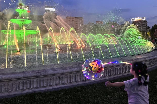 A girl plays with a balloon at a city fountain in Bucharest, Romania