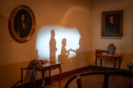 Shadow silhouettes of three people projected on a museum wall between framed portraits