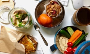 Le pack de déjeuner de bureau de Jackie Middleton, sur un bureau avec salade de pâtes aux pois, poulet et pesto, sandwich au fromage cheddar pré-grillé, crudités et houmous à tremper, un mini muffin et des fruits de saison
