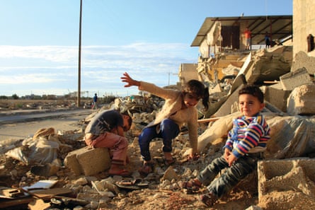 Children sit in front of their destroyed house in Khuza’a