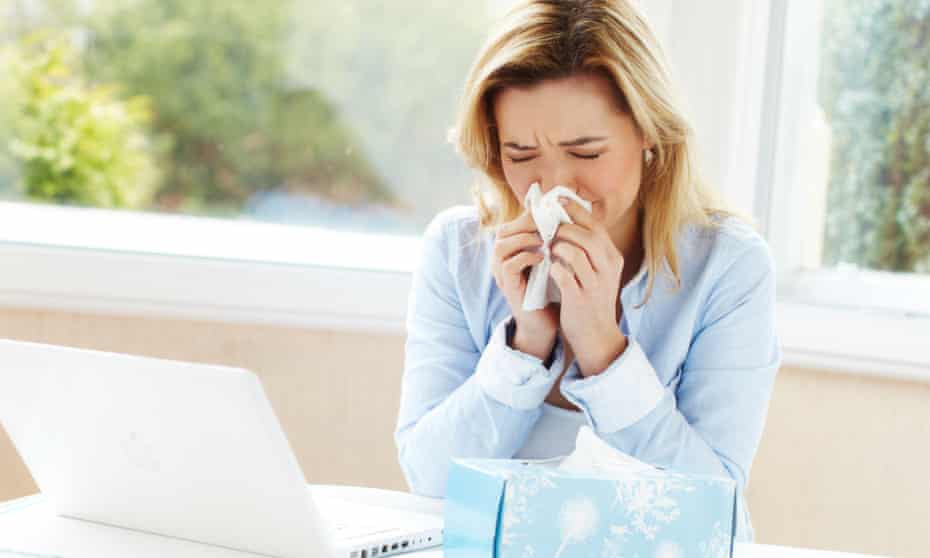 Woman with cold blowing nose in front of a laptop