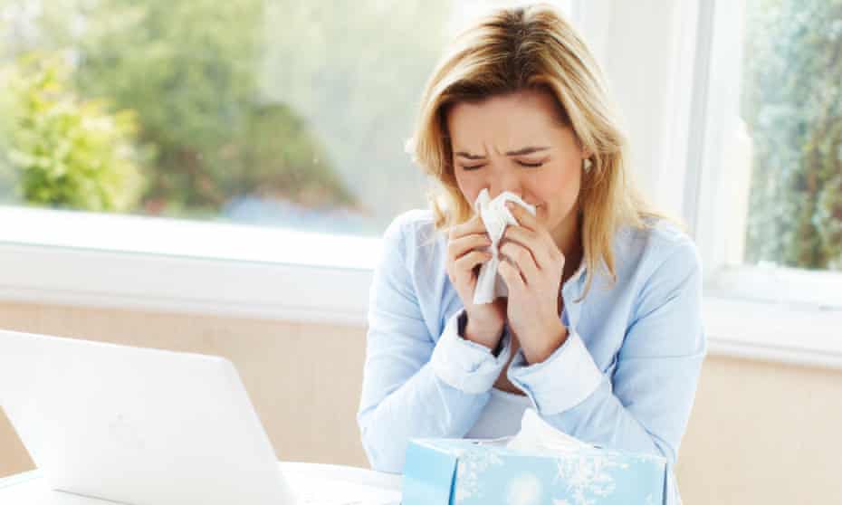 woman with cold blowing nose at her work desk