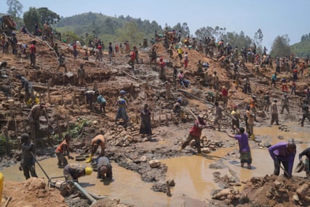 People digging and panning in muddy water at an open-cast goldmine.