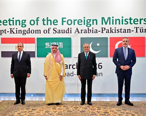 The four ministers stand in a row in front of their countries' flags