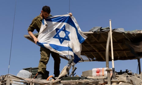 A soldier hangs an Israeli flag on an armoured personnel carrier near the border with Gaza