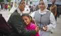 A distressed Arab woman in a headscarf comforts a crying Arab girl as another woman looks on