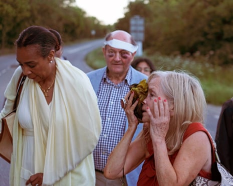 A woman in an orange top is injured after a train crash and stands with other people nearby on a roadside