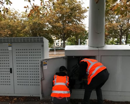 Back of two people in orange hi-vis vests at open cabinet door outside