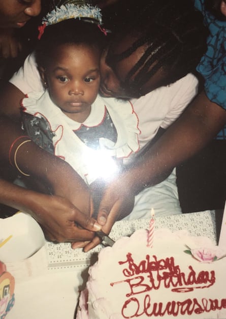 A baby girl sits on the lap of an older girl who is cutting her birthday cake