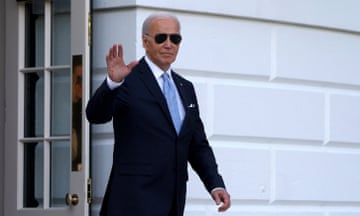 Older white man, dark suit, aviator sunglasses, waves as he departs a white building.