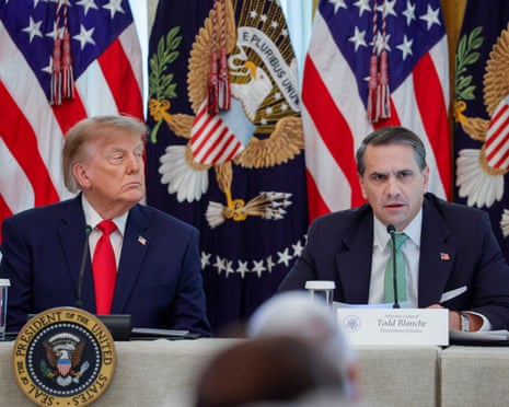 Donald Trump, wearing a blue suit, looks to the side while seated at a table with Todd Blanche, also in a blue suit, who is speaking
