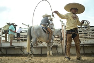 A boy wearing a wide-brimmed hat, shirt and chaps over his jeans whirls a lasso