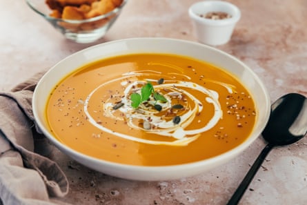 A bowl of pumpkin soup with a swirl of cream on top and green garnish.