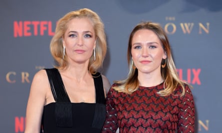 Gillian Anderson, with long blonde hair and long silver earrings and a black dress, standing with her daughter, who is also blonde and wearing a red and black dress
