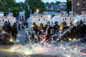 Firecrackers go off in front of riot police officers gathered behind their vans with a barricaded crowd in the distance