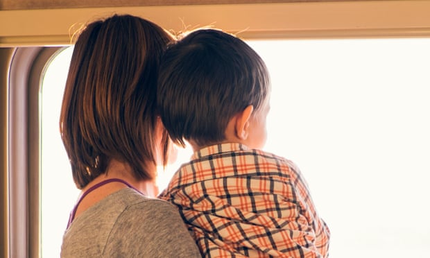 Rear view of woman and toddler son looking out of sunlit train window