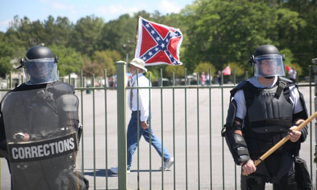 A man waves a Confederate flag in front of riot police.