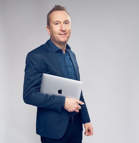 Man in blue suit holding an Apple laptop under one arm