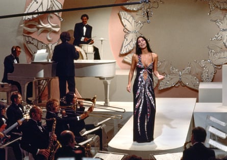 A woman wearing a sparkly illusion dress on a TV set with an orchestra
