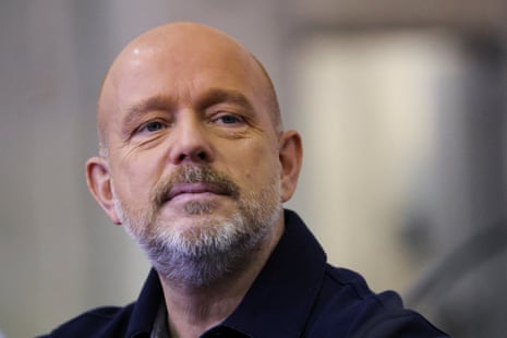 Steve Hilton, bald with a grey beard, wears a dark polo shirt with a neutral expression