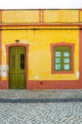 A bright yellow house with a wooden door with wrought iron grills