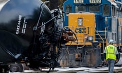 A locomotive in front of an upended tanker car with a CSX employee walking by.