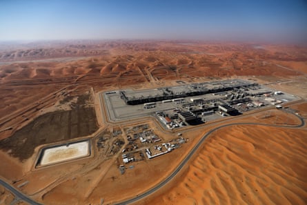 General aerial view of Aramco’s oilfield buildings set in an expanse of flat, orange, sandy desert against a blue sky.