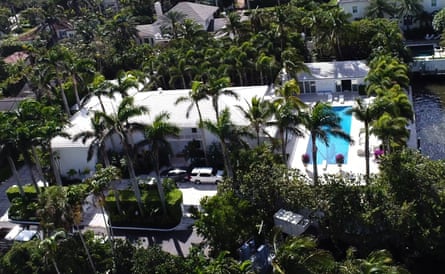 a large white home with a blue pool surrounded by green palm trees