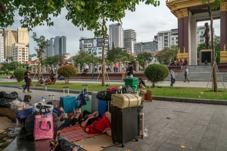 People sit or lie among piles of luggage on the roadside in a city