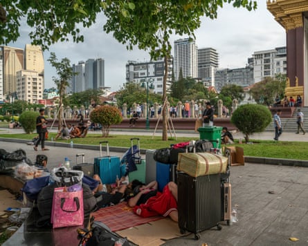 People lie on mats on a pavement, surrounded by suitcases and bags