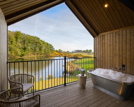 A metal bathtub full of bubbles sits on a cabin deck overlooking a lake at Tempus Northumberland