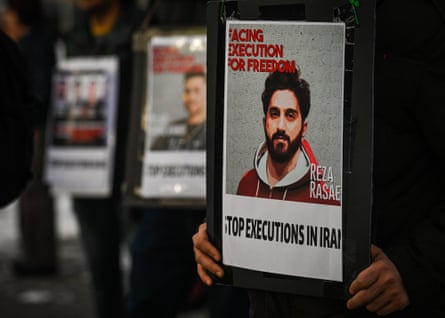 A row of people holding posters. The poster in the foreground shows a photo of Reza Rasaei with the words ‘Facing execution for freedom’ and ‘Stop executions in Iran’