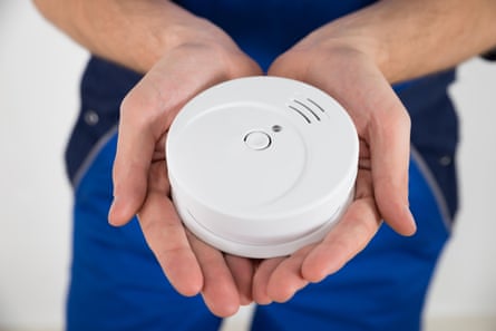 A closeup image of a male electricianâÂÂs two hands holding a white smoke detector .