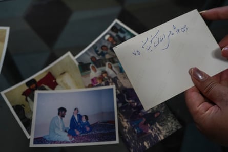 Hands hold a photograph with its back on show, covered with writing, over a pile of other photographs.