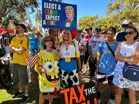 a group stands together at protest, two in toy story and spongebob squarepants costumes, and others holding signs such as ‘elect a clown, elect a circus’ and ‘tax the rich’