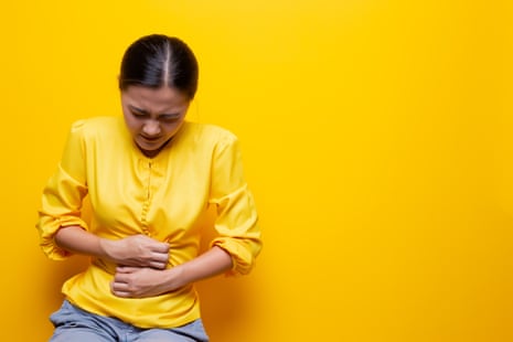 Woman with a stomachache standing against a yellow background.
