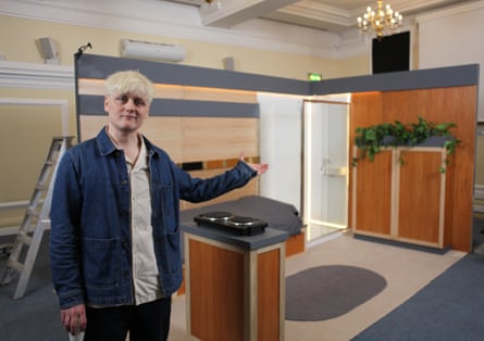 Looking at the camera, he gesticulates towards a boxy room about the size of a room in a university dormitory