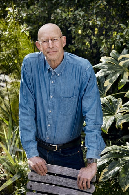 Michael Pollan in a blue Oxford shirt, standing up, leaning on a garden chair