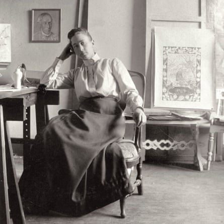 Hilma af Klint sitting at a desk with artwork on the wall and resting on furniture behind her
