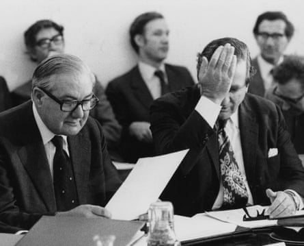 The two men sit at a table with Healey doing what looks like a facepalm