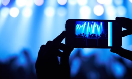 Uma pessoa filma sua banda favorita com um celular com câmera.