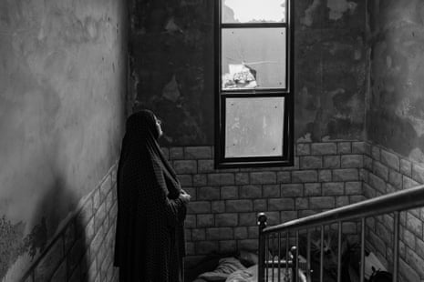 A woman looks out of a broken window