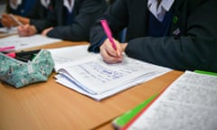 Headless view of children in school uniforms writing in school exercise books