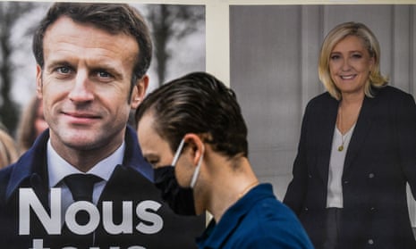 person walks in front of poster of macron and le pen