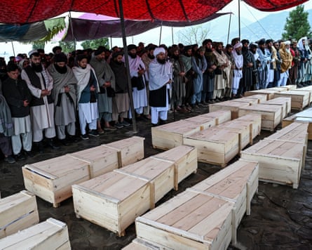People stand to offer prayers with rows of coffins lined up in front of them