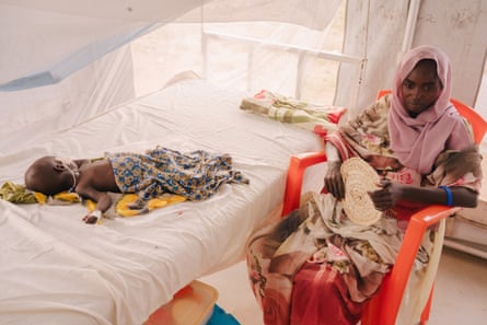 A woman sits by a hospital bed that has a small child lying on it
