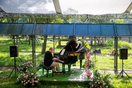 Rick Wakeman plays piano flanked by two large speakers to the backdrop of a fenced-off bear sanctuary.