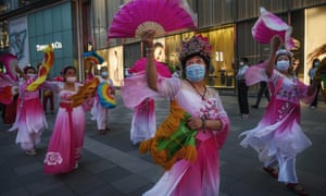 Chinese women wear protective masks and costume as they dance for exercise outside a luxury shopping mall on 4 June 2020 in Beijing.