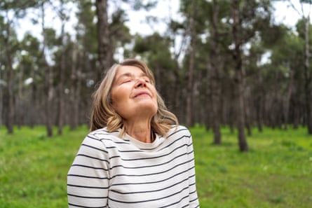 Mature woman enjoying the tranquility of a green forest, breathing deeply with closed eyes, embracing the peace of natureMature woman experiencing forest tranquility, breathing deeply with closed eyes, connecting with peaceful wilderness surroundings