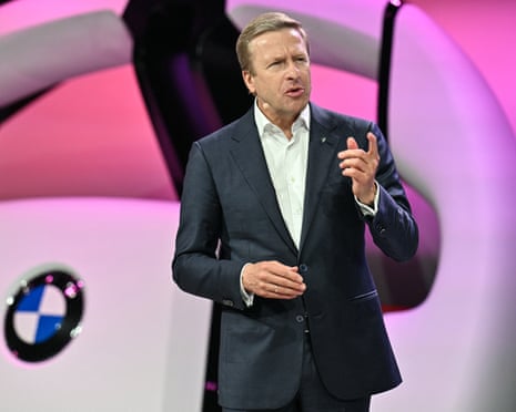 Oliver Zipse speaking at a conference in front of a large image of a BMW steering wheel